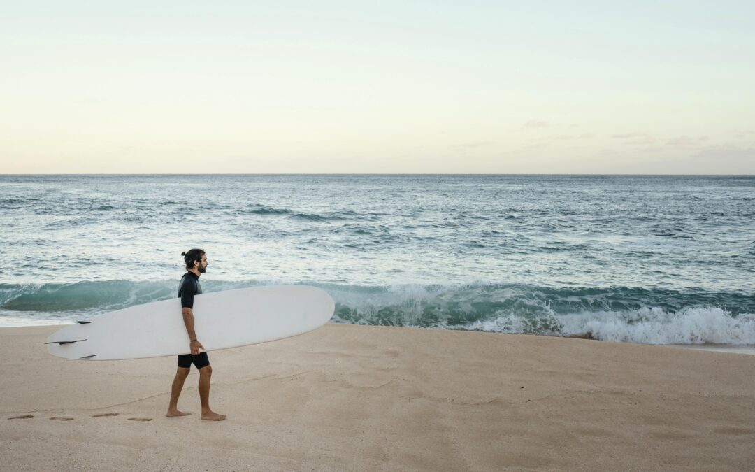 Homem caminhando pela praia com a sua prancha de surfe.